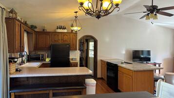 A kitchen with wooden cabinets, a black refrigerator, a microwave, a stove, and a ceiling fan.