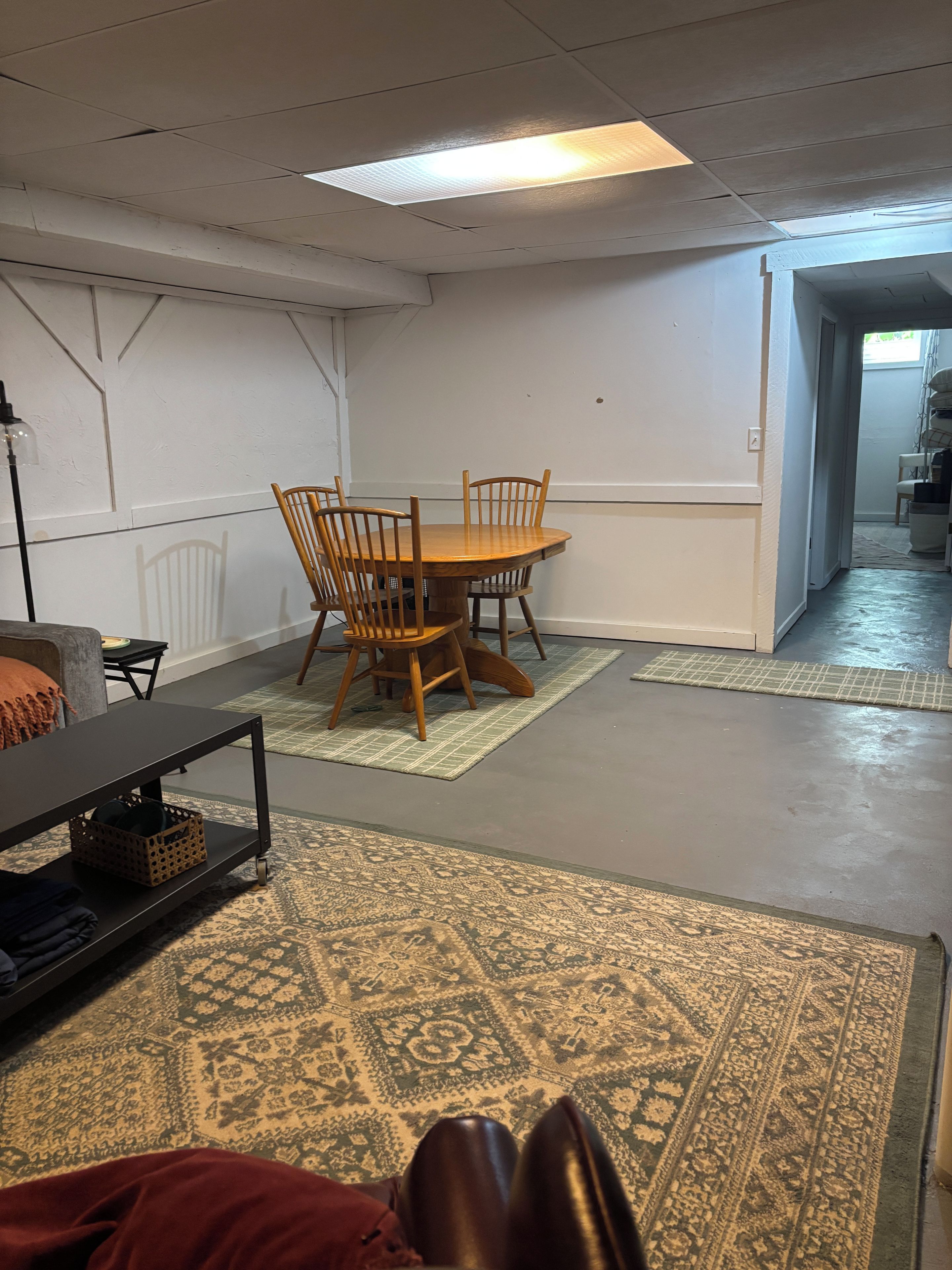 Una habitación con una mesa redonda de madera, cuatro sillas, una lámpara de mesa negra y alfombras estampadas en el suelo.