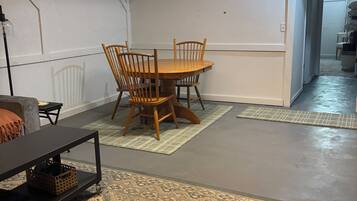 Una habitación con una mesa redonda de madera, cuatro sillas, una lámpara de mesa negra y alfombras estampadas en el suelo.