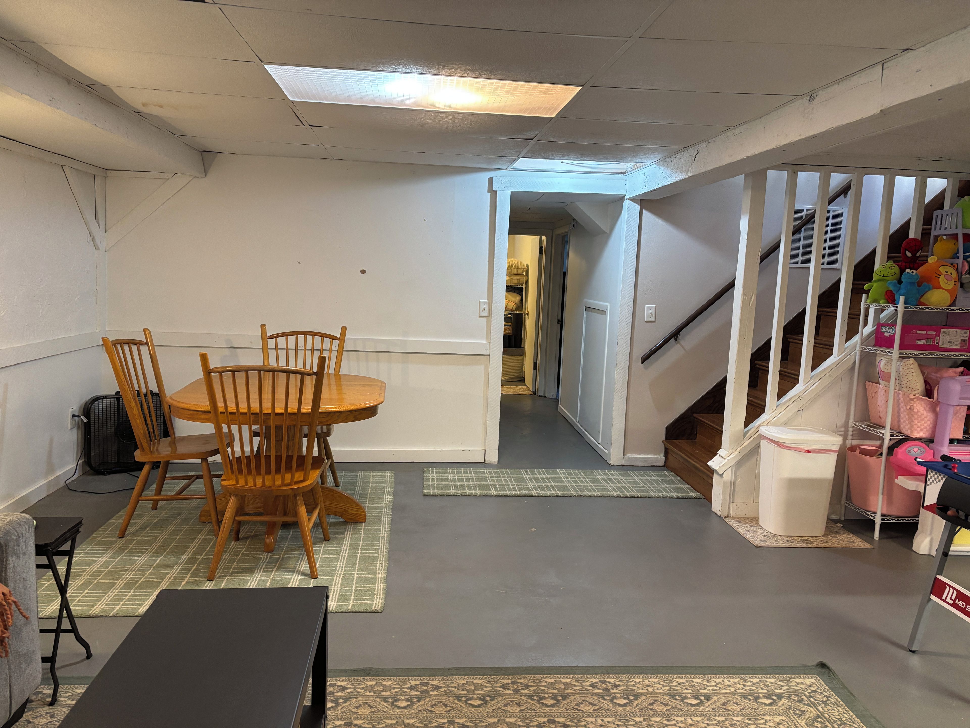 Ein Zimmer mit Esstisch, Stühlen, einem schwarzen TV-Schrank, einem Ventilator und einer Treppe mit einem Spielzeugregal.