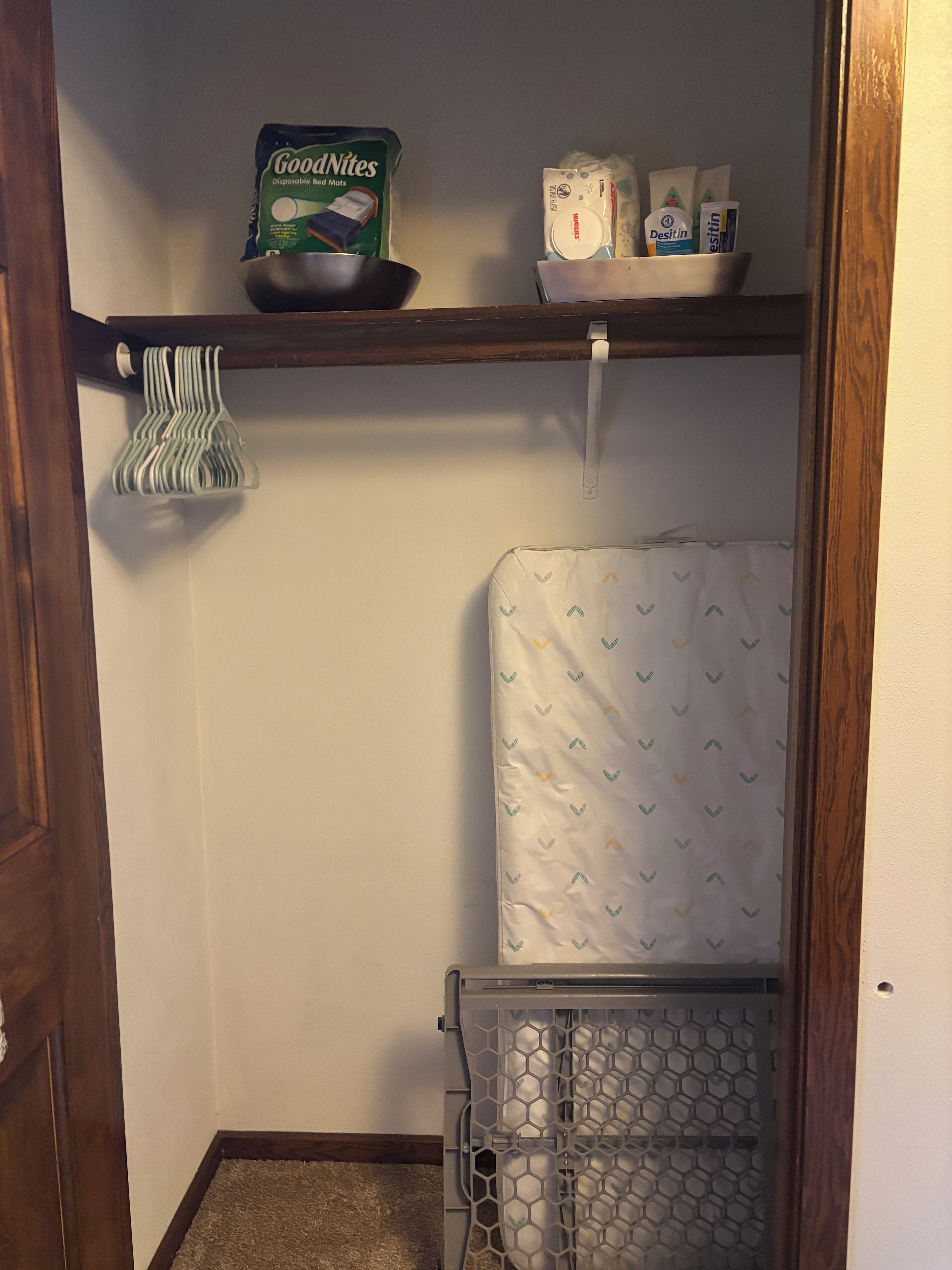 A laundry room with a shelf holding GoodNites disposable bed mats, Desitin diapers, and a basket of laundry.
