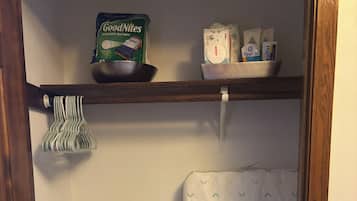 A laundry room with a shelf holding GoodNites disposable bed mats, Desitin diapers, and a basket of laundry.