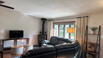 Una sala de estar con un sofá de cuero, televisor, chimenea y una ventana con cortinas.