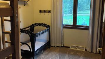 A child's room with bunk beds, a crib, a window with curtains, and a rug with a dinosaur design.
