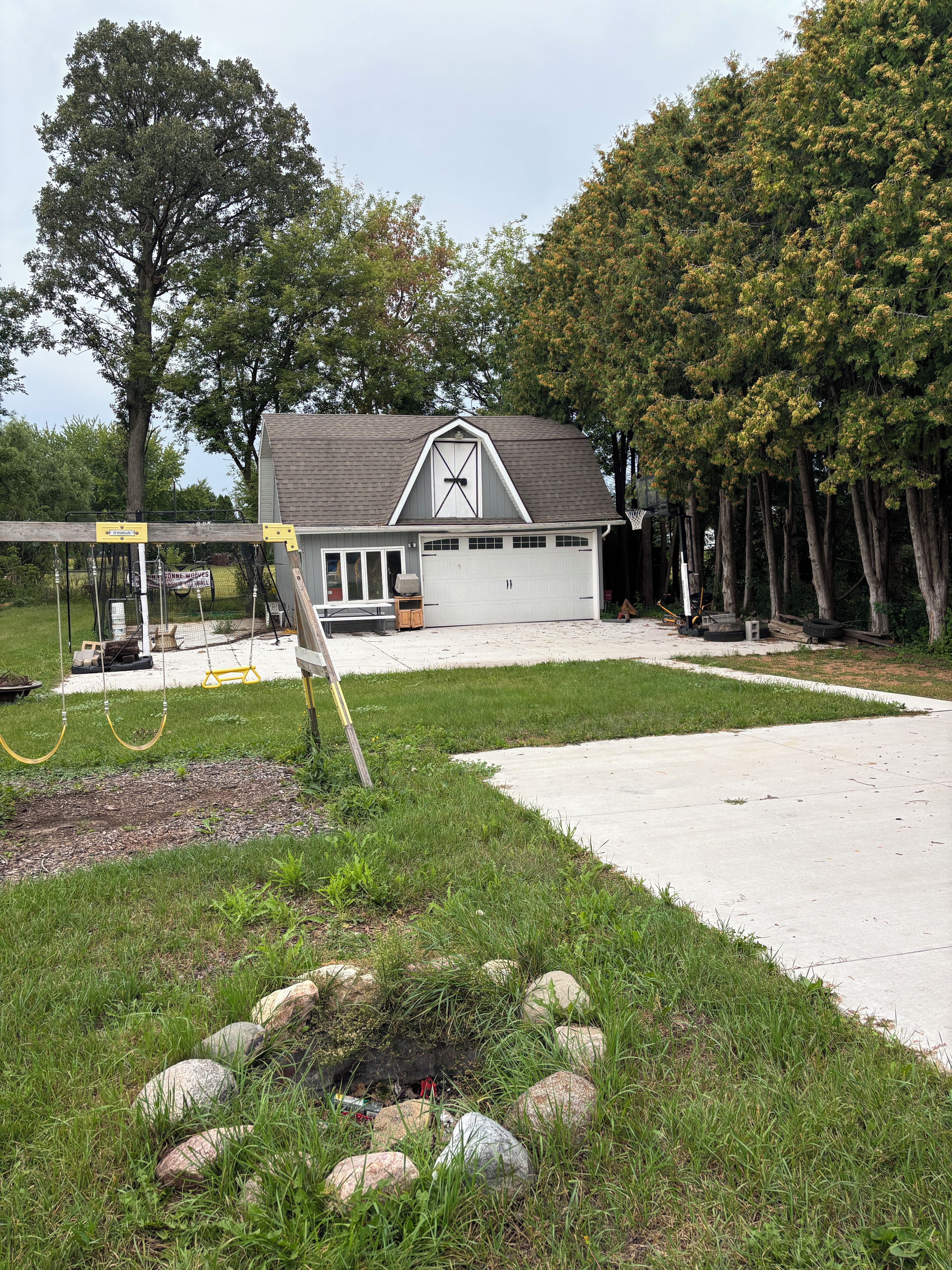 A residential garage with a sloped roof, a covered porch, and a driveway leading to a house.