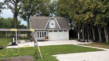 A residential garage with a sloped roof, a covered porch, and a driveway leading to a house.