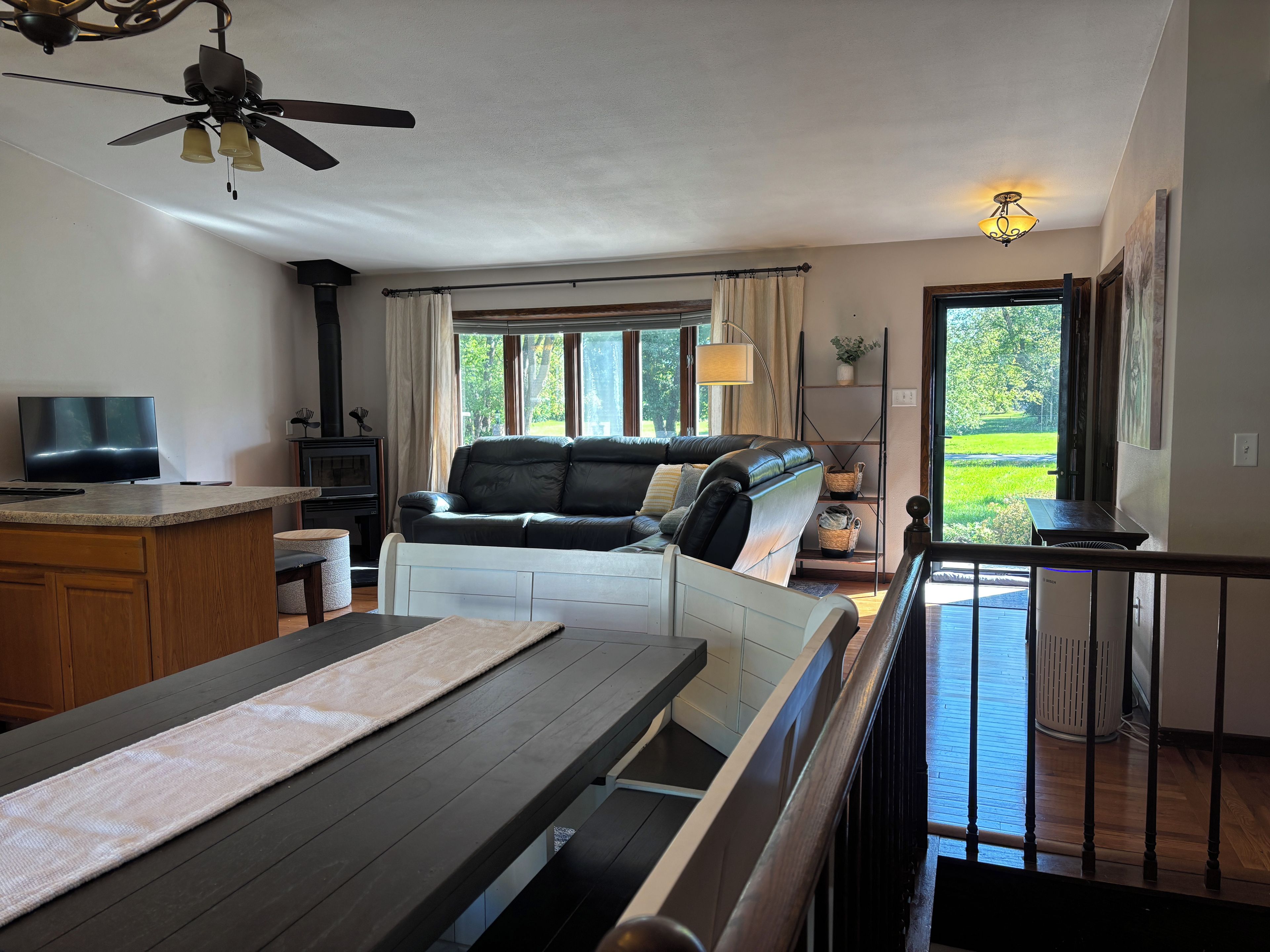 A living room with a sofa, a TV, a ceiling fan, and a view of the outdoors.