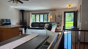 A living room with a sofa, a TV, a ceiling fan, and a view of the outdoors.