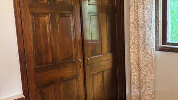 A room with a large wooden wardrobe, a window with patterned curtains, and a carpeted floor.