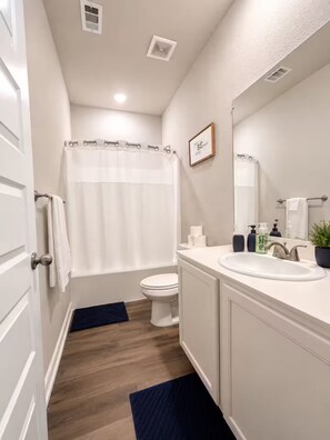 A bathroom with a toilet, sink, and shower curtain. - Bell Station Executive Cottage •Ground‑Level 1BR (Hurst)