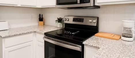 Una cocina con armarios blancos, un microondas de acero inoxidable, una estufa y una cafetera.