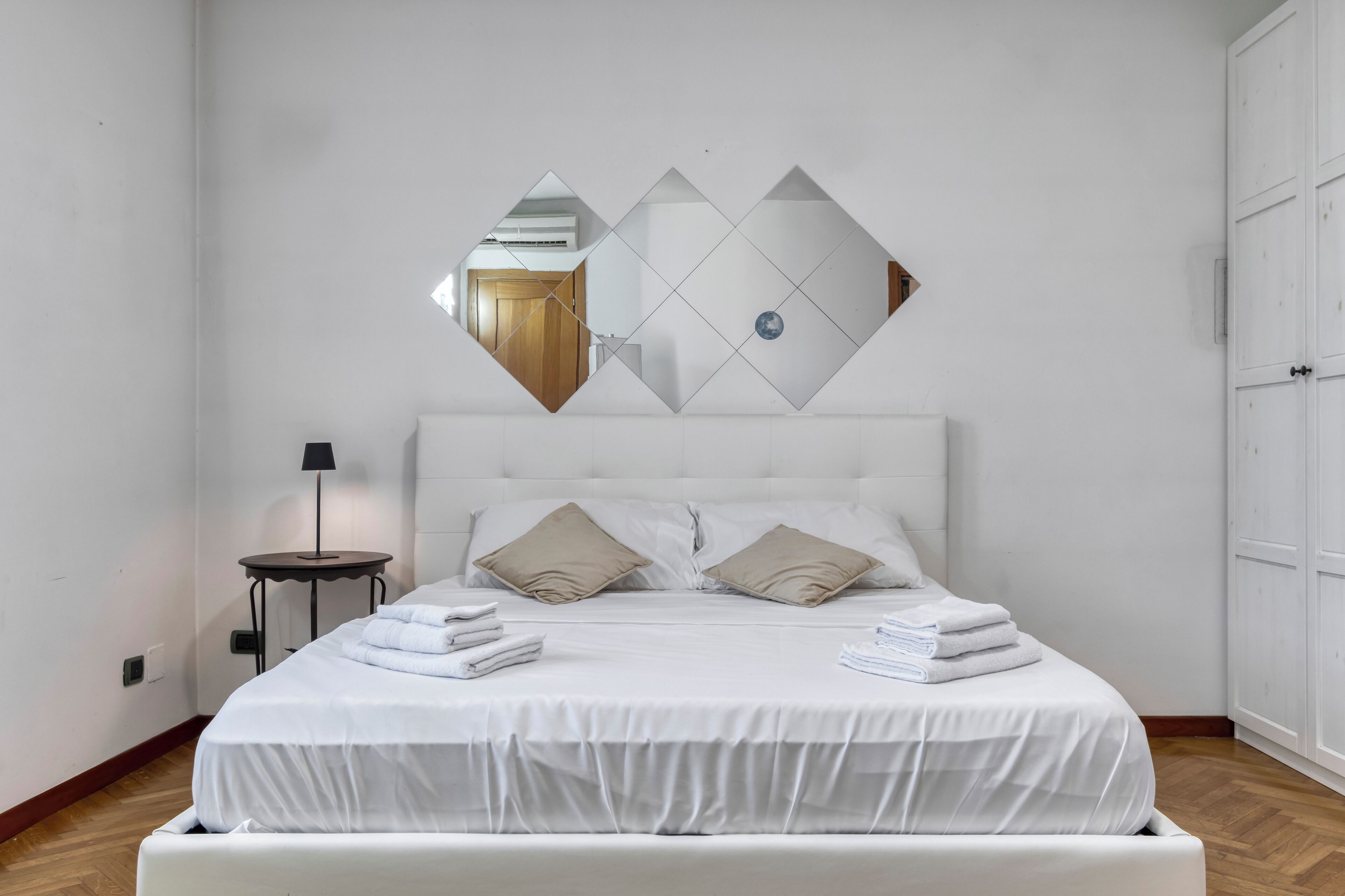 Una camera da letto con un letto, due cuscini, un comodino con una lampada e uno specchio a parete.