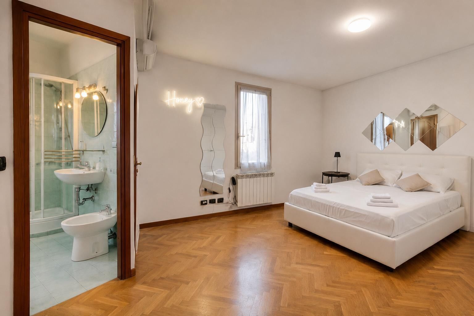 A bedroom with a bed, a bedside table, a mirror, and a window.
