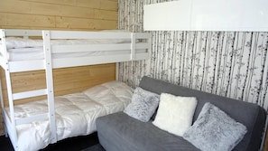 Ein Stockbett mit weißer Bettwäsche und ein graues Sofa mit flauschigen Kissen vor einer Wand mit Tapete.