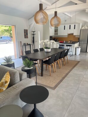 Een moderne keuken met witte kastjes, een roestvrijstalen koelkast en een eethoek met een donkere tafel en stoelen.