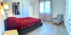 Ein modernes Schlafzimmer mit einem Bett, einem Sessel, einer Wandlampe und einem Fenster mit Vorhängen.