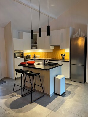 Une cuisine moderne avec des meubles blancs, un réfrigérateur en acier inoxydable, un plan de travail noir et un pare-feu jaune.