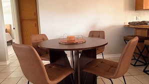 Uma sala de jantar com uma mesa redonda e quatro cadeiras, um armário de madeira e piso ladrilhado.