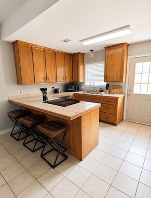 A kitchen with wooden cabinets, a central island with stools, a microwave, and a sink. - 4BR/2BA – Flexible Queen & Twin Sleeping – Quiet Neighborhood (Abilene)