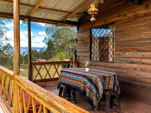 A wooden cabin with a covered porch, a table with a colorful tablecloth, and a view of the surrounding landscape.