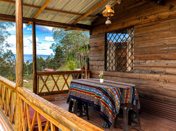 A wooden cabin with a covered porch, a table with a colorful tablecloth, and a view of the surrounding landscape.