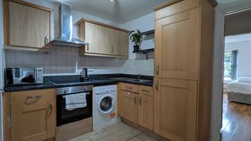 A modern kitchen with wooden cabinets, a built-in oven, a washing machine, and a microwave.