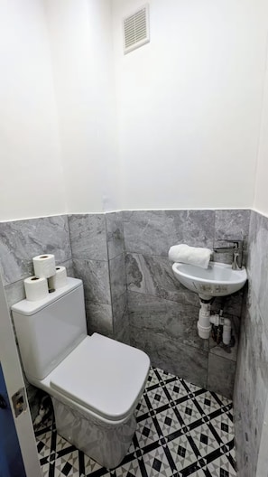 A small bathroom with a toilet, a sink, and marble tiles. - House Sleeps 5 With Parking and Garden (Feltham)