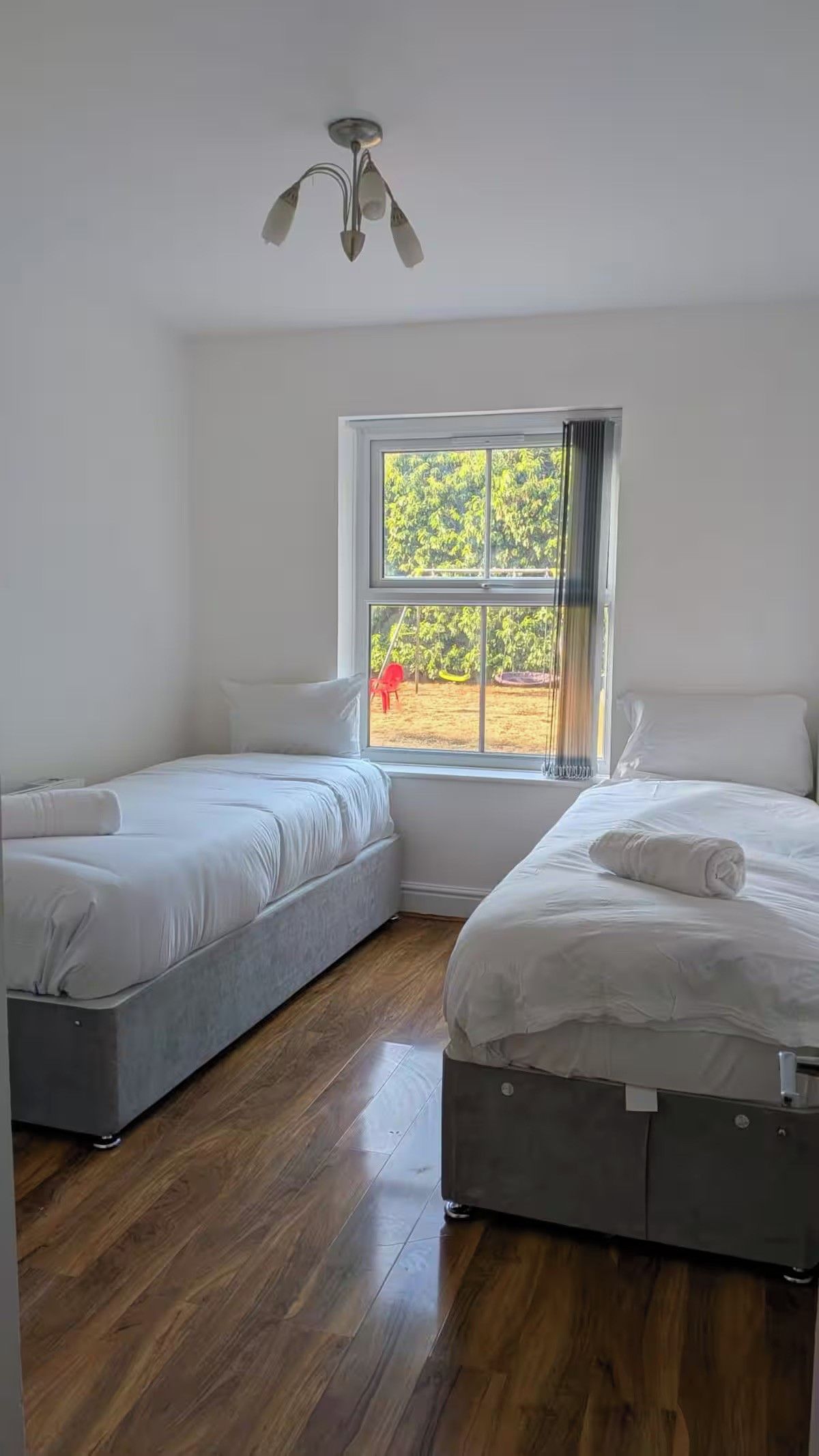 Quarto com duas camas, janela com vista para o verde e luminária no teto.