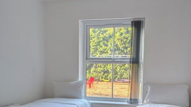 A room with two beds, a window with a view of greenery, and a ceiling light fixture. - House Sleeps 5 With Parking and Garden (Feltham)