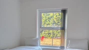 Quarto com duas camas, janela com vista para o verde e luminária no teto.