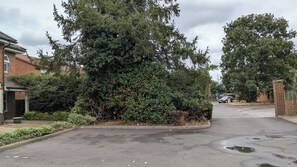 Una calle residencial con casas, un coche aparcado y un árbol grande al frente.
