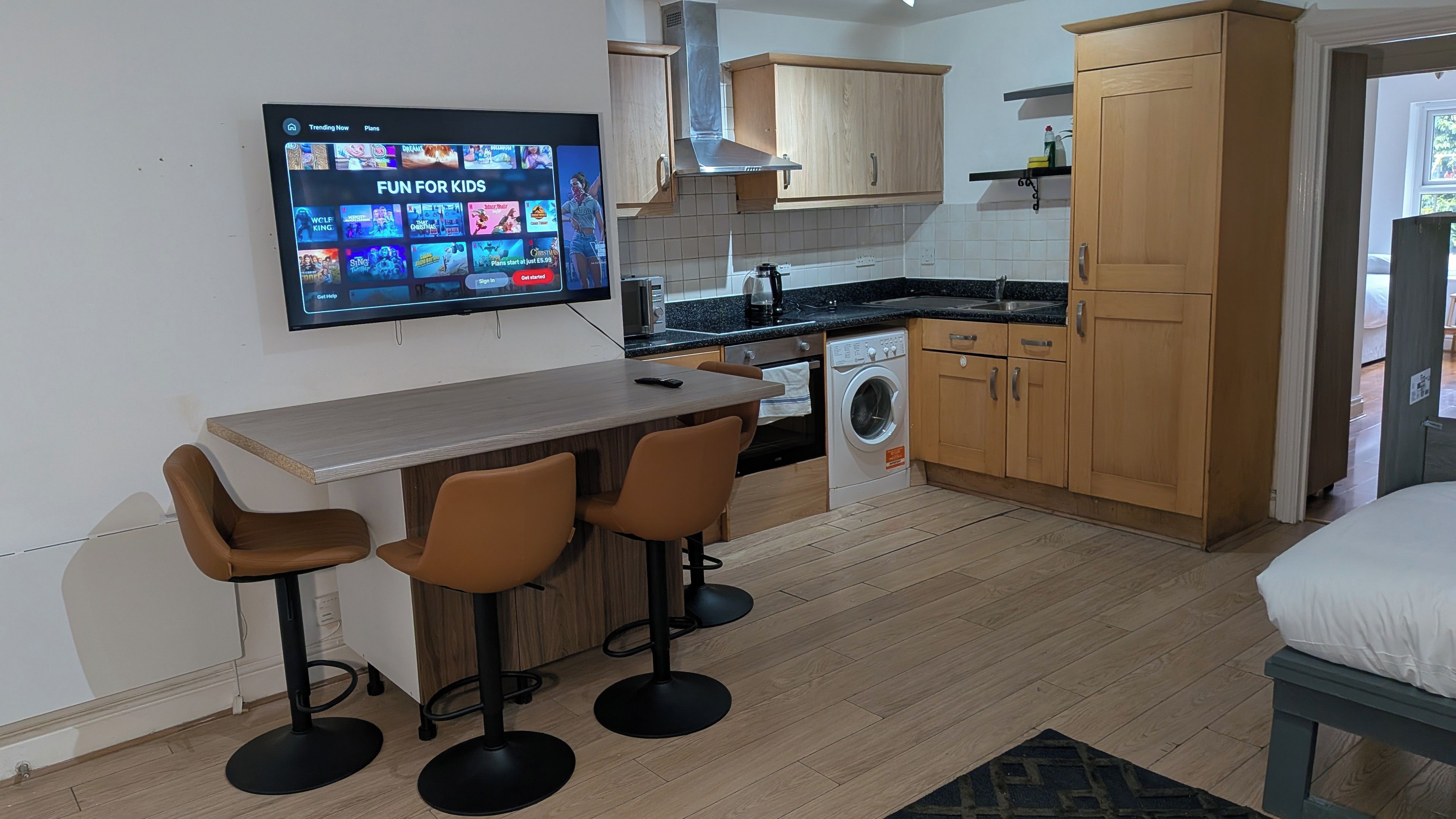 A compact kitchen with a dining area, a washing machine, and a TV displaying a children's channel.