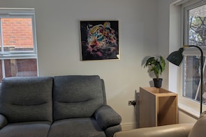 Una sala de estar moderna con un sofá gris, una mesita de madera con una planta, una lámpara de pie negra y un cuadro abstracto colorido en la pared.
