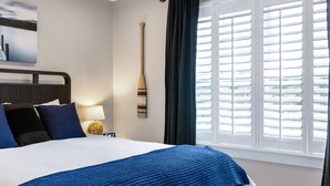Een hotelkamer met een bed, nachtkastje, lamp, schilderij aan de muur en een raam met zonwering.