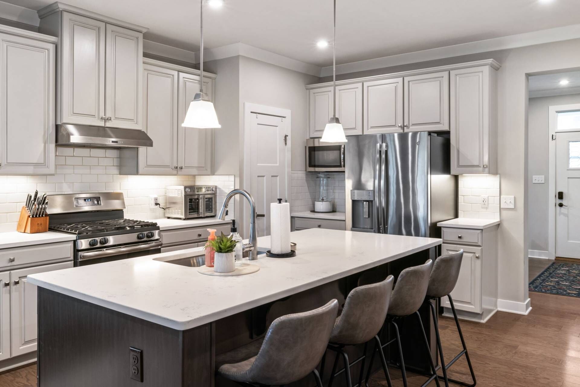 A modern kitchen with white cabinetry, stainless steel appliances, and a central island with bar stools.