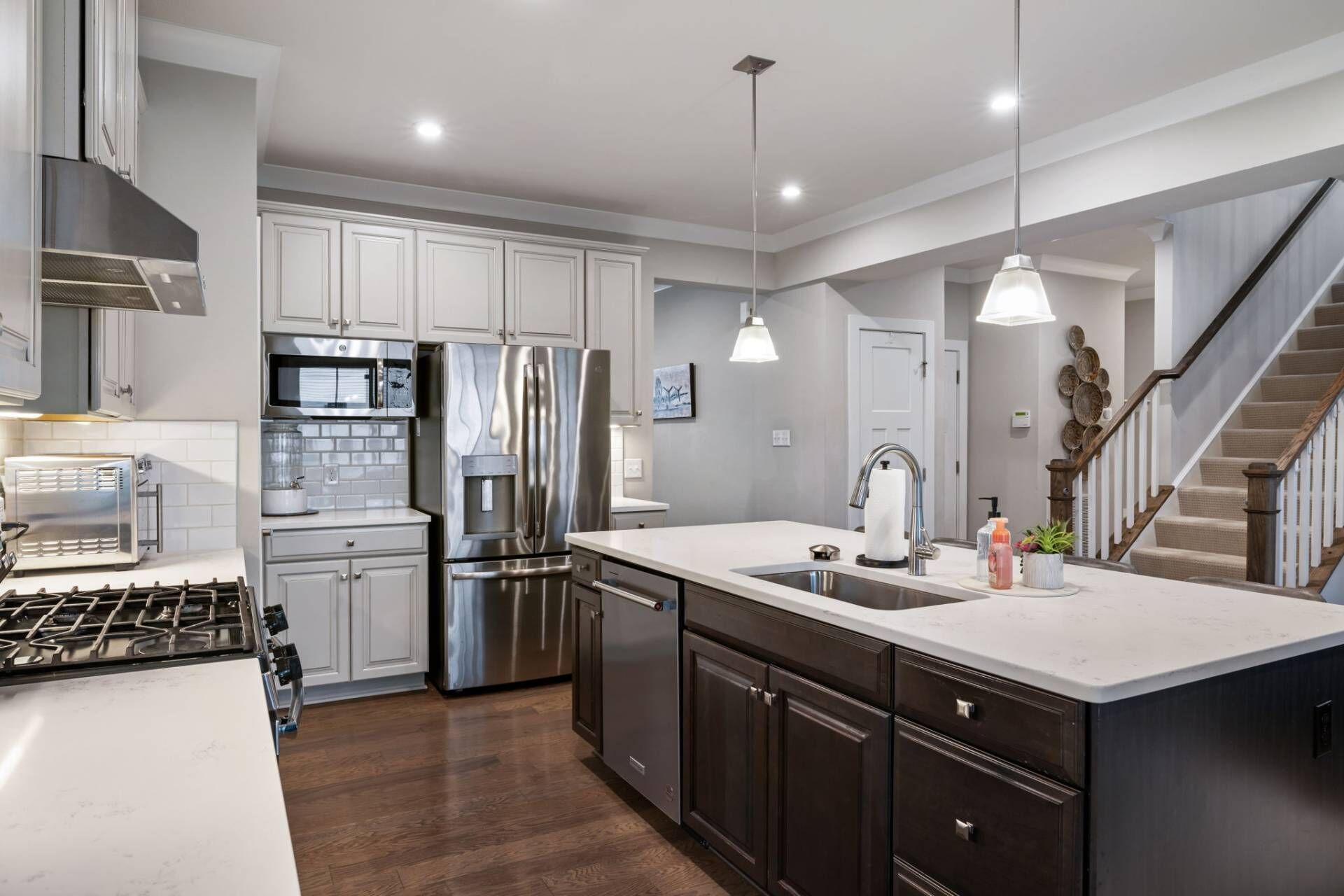 A modern kitchen with stainless steel appliances, a large island, and a staircase leading to another level.