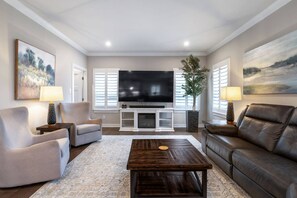 A living room with a flat-screen TV, two armchairs, a sofa, a coffee table, and two lamps.