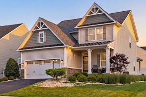 A two-story house with a garage, a covered porch, and a well-maintained lawn. - Wings of Steel - 4BR Plus Bunk Room, Hot Tub, Fire Pit Table, 20 Minutes from Downtown Pittsburgh (Plum)