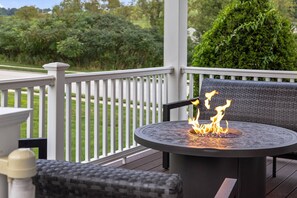 A round outdoor table with a built-in fire feature, surrounded by wicker furniture and a white railing.
