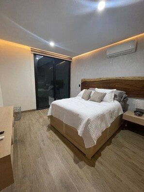 Quarto moderno com uma cama grande, uma escrivaninha e uma porta de vidro deslizante para uma varanda.