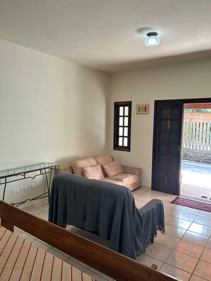 Ein Zimmer mit einer Couch, einer Bank, einem Glastisch, einer Tür und Blick ins Freie.