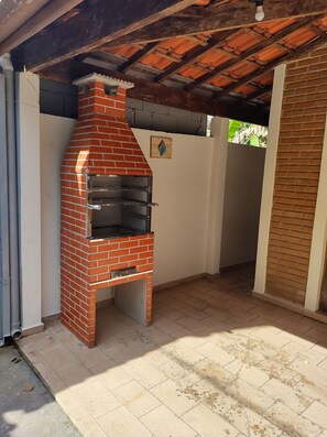 A brick-built outdoor oven structure with a chimney, a tiled floor, and a partial view of a building's interior. - Vacation home in Ubatuba, SP (Ubatuba)