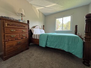 A bedroom with a wooden dresser, a bed with a green bedspread, a window with daylight, and a ceiling with a textured finish. - Spacious 4-bedroom house with AC in enchanting Columbus (Columbus)