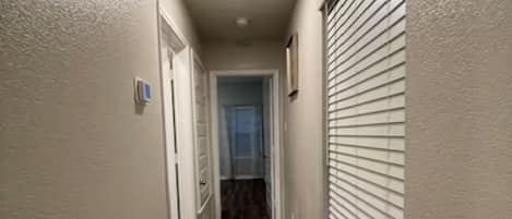 Un pasillo con piso de madera, paredes blancas y una puerta al final.