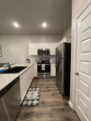 A compact kitchen with white cabinets, stainless steel appliances, and a checkered doormat. - Cozy 1BR Cottage Retreat Ideal for Extended Stays (Hurst)