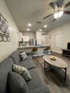Ein modernes Wohnzimmer mit einem grauen Sofa, einem Holztisch und einem Deckenventilator.