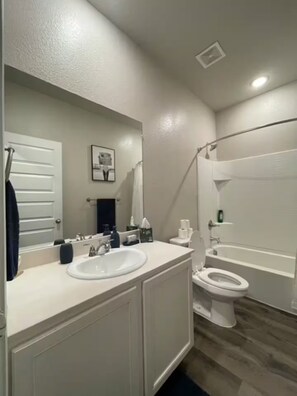 A bathroom with a white sink, mirror, and toilet. There is a shower curtain and a towel rack. - Cozy 1BR Cottage Retreat Ideal for Extended Stays (Hurst)