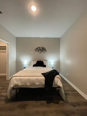 A bedroom with a bed, a wall-mounted light fixture, and a door. - Cozy 1BR Cottage Retreat Ideal for Extended Stays (Hurst)