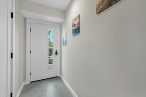 Un couloir avec une porte blanche, une petite fenêtre et deux tableaux encadrés accrochés au mur.