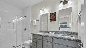 A modern bathroom with a walk-in shower, a toilet, a vanity with a granite countertop, and a large mirror. - Superb Southside Townhome (Asheville)